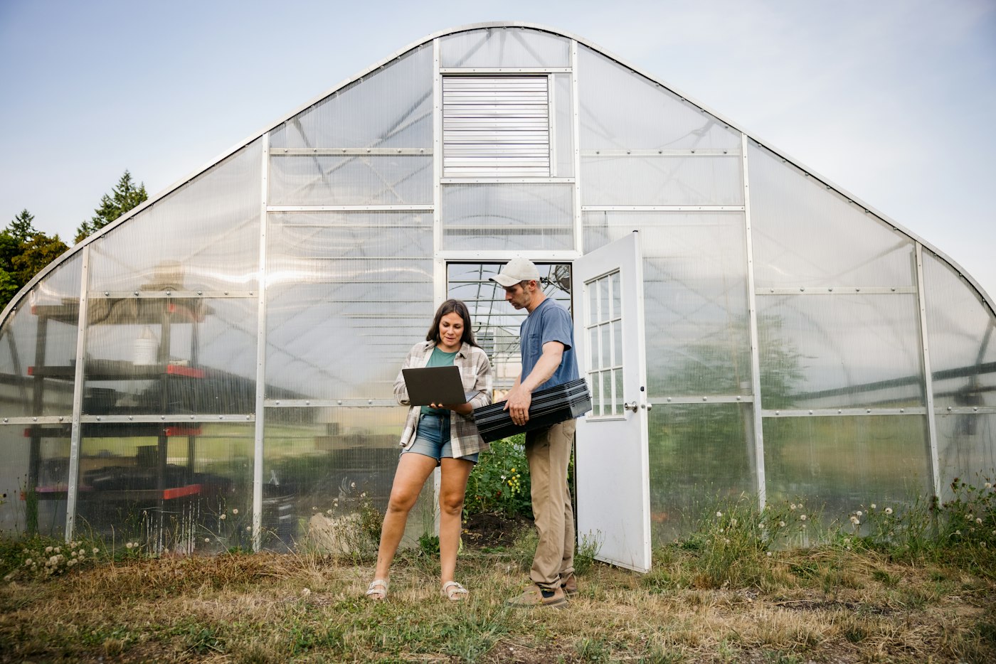 Two farm operators reviewing records on a laptop outside a greenhouse