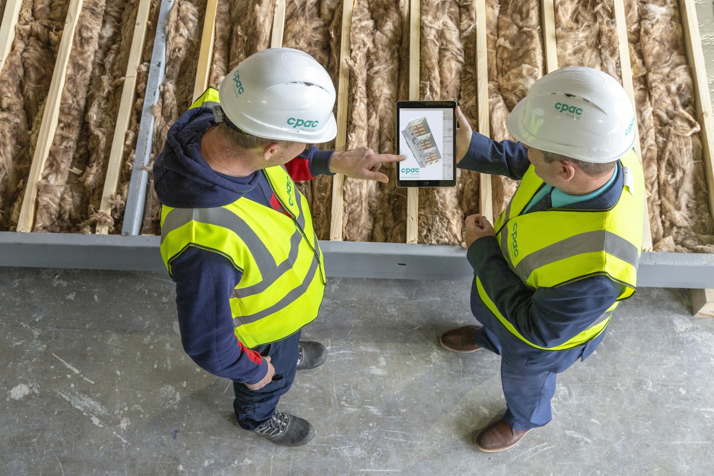Two workers in hard hats reviewing plans on a tablet on site