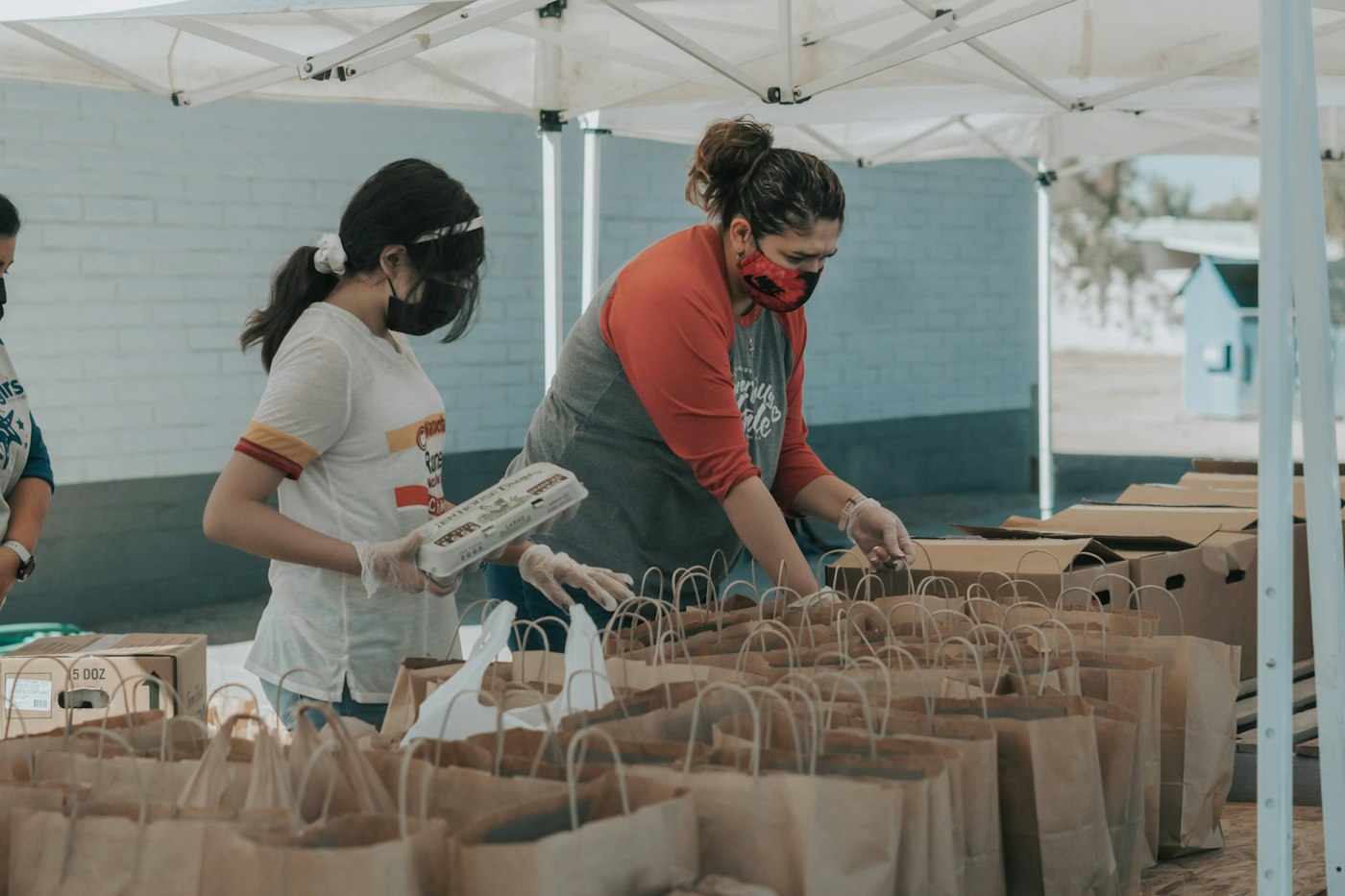 Two volunteers packing paper bags under a canopy