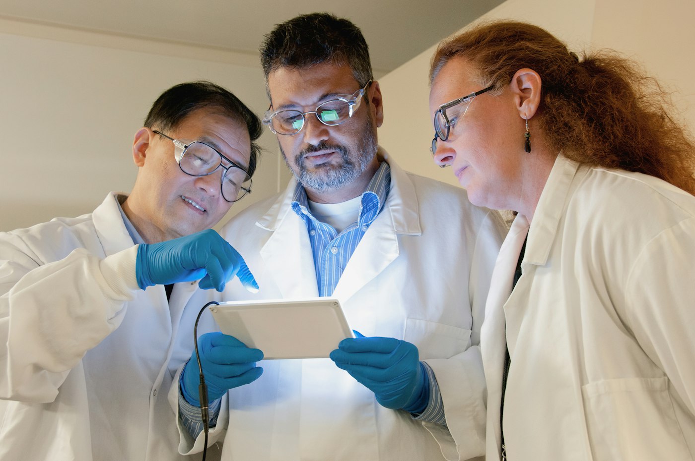 Three researchers in lab coats reviewing information on a tablet